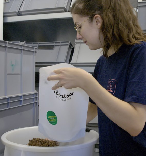 Eine Mitarbeiterin der roestbar Münster füllt frischen Kaffee in eine Verpackung